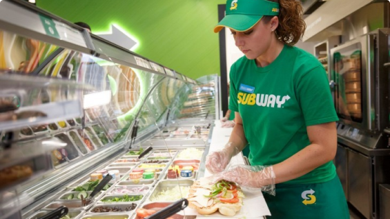 Sandwich Artist making a footlong sub for a customer.
