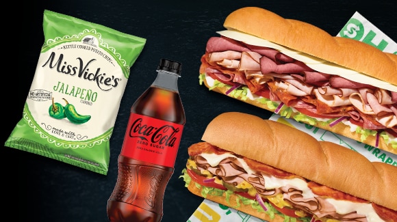 Chips and bottled drink next to two footlongs.