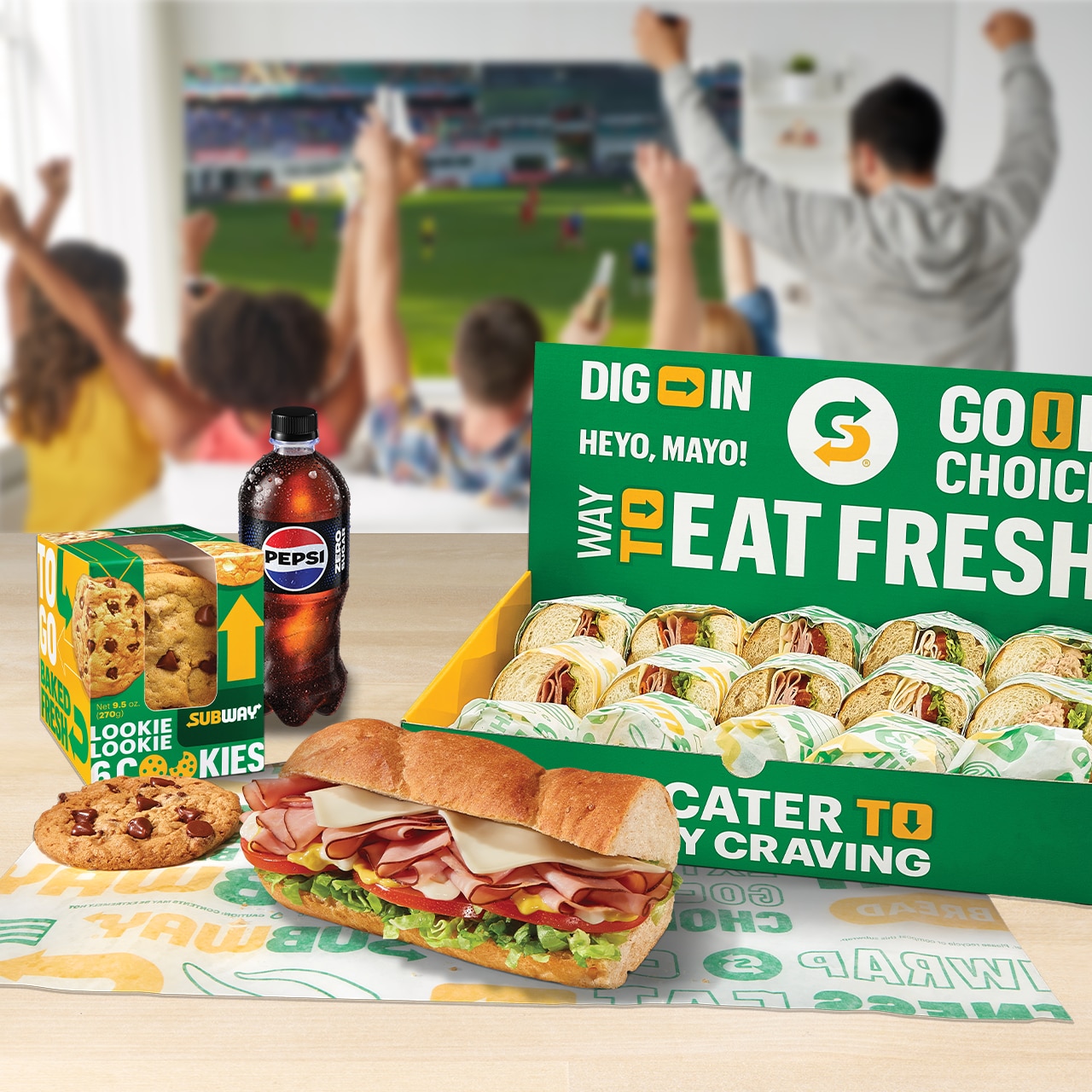 Subway catering box with an unwrapped sub, chips and cookie nearby.